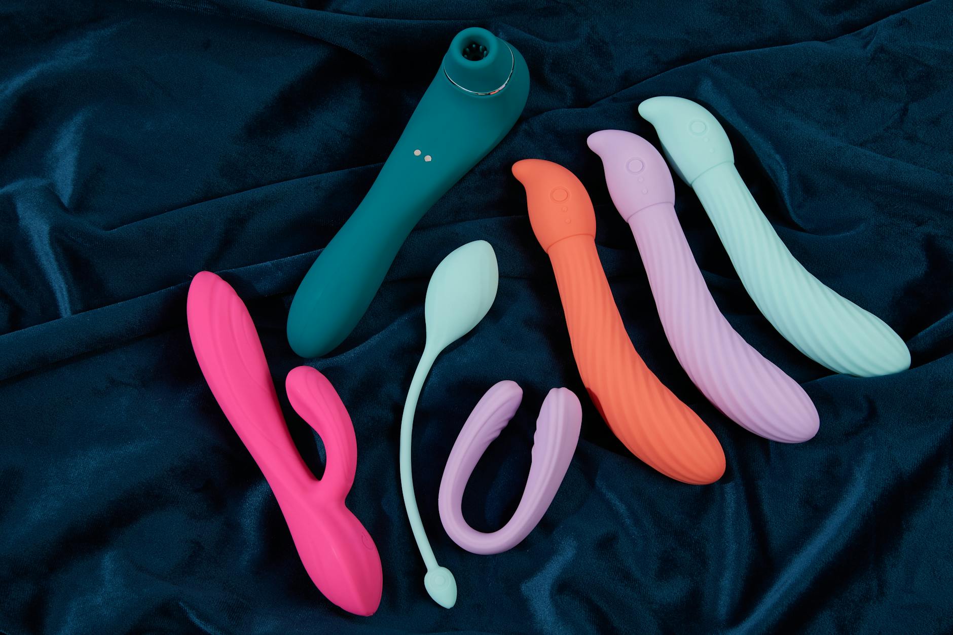 A hand reaching over a variety of colorful sex toys arranged on a table, symbolizing choice and intentional intimacy