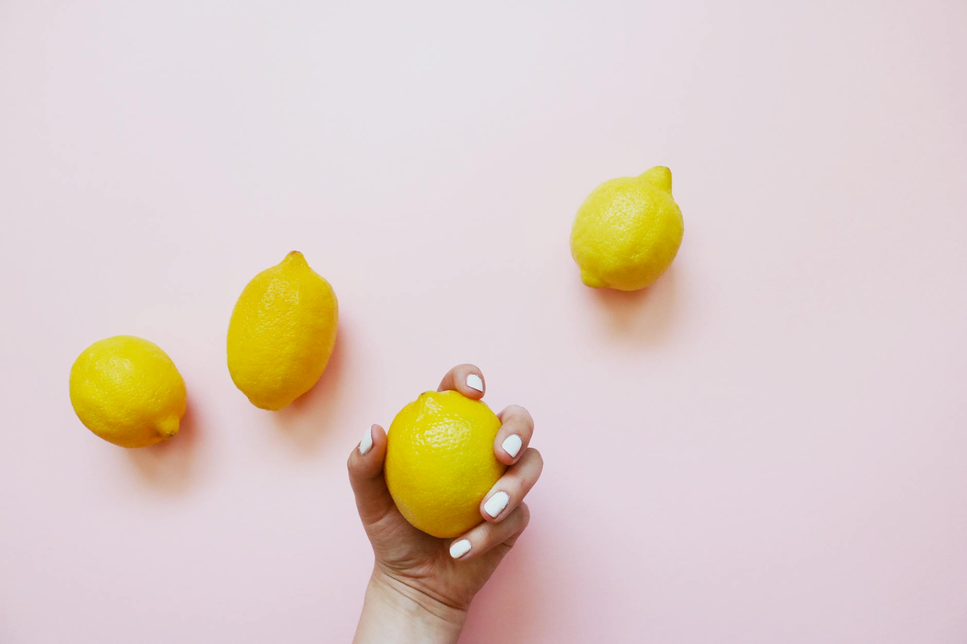A hand holding a fresh lemon on a soft pink background, symbolizing self-care and intimacy