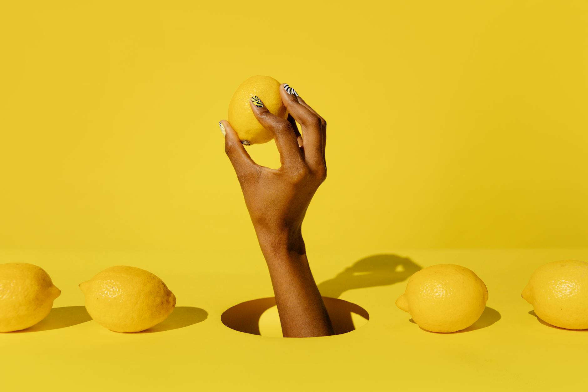 A hand holding a fresh lemon against a vivid yellow background, symbolizing renewed sensory experience and freshness