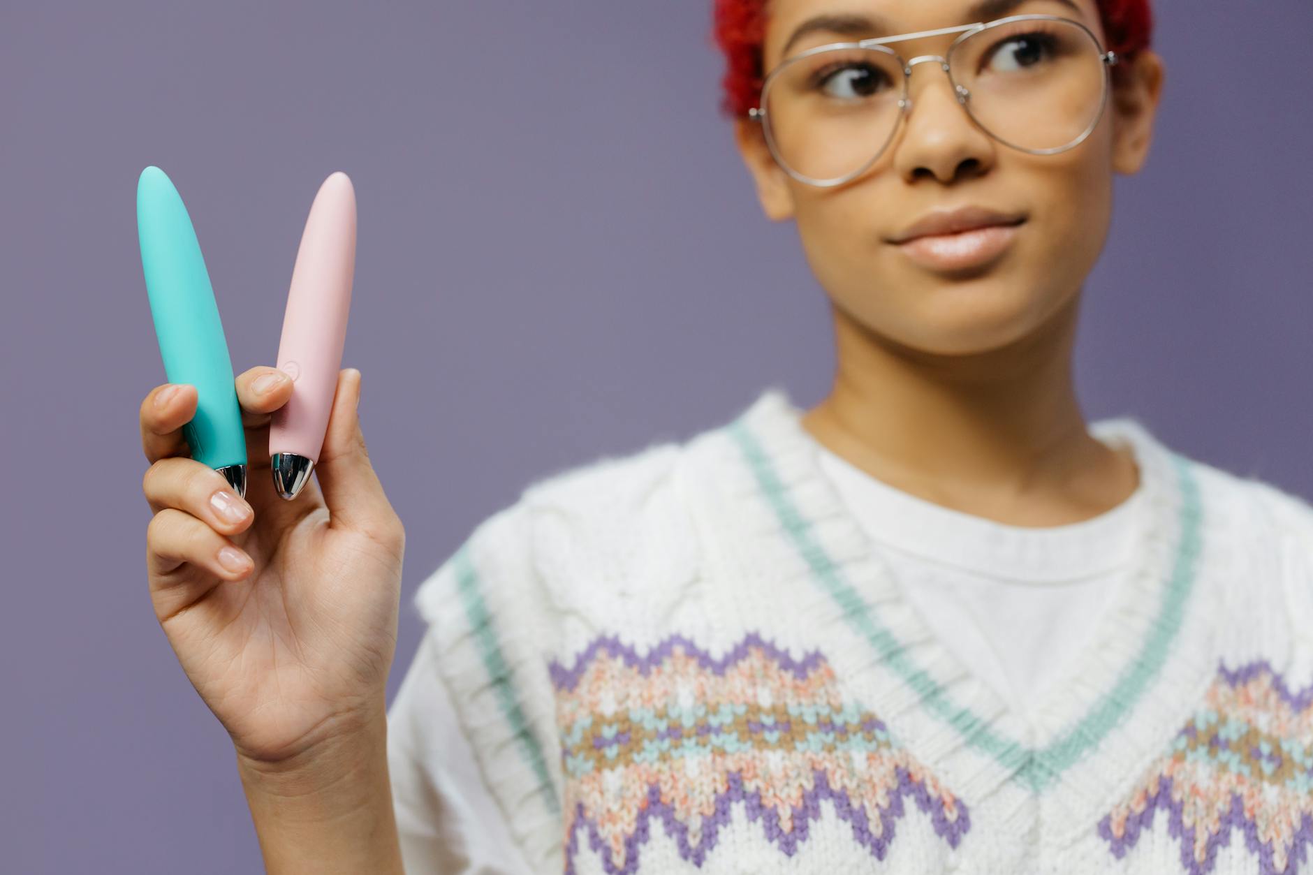Person holding vibrators against a purple background, symbolizing pleasure and self-care.