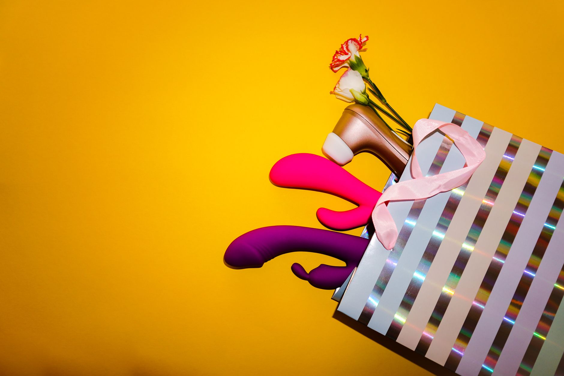 Colorful vibrators with flowers in a holistic gift bag on yellow background